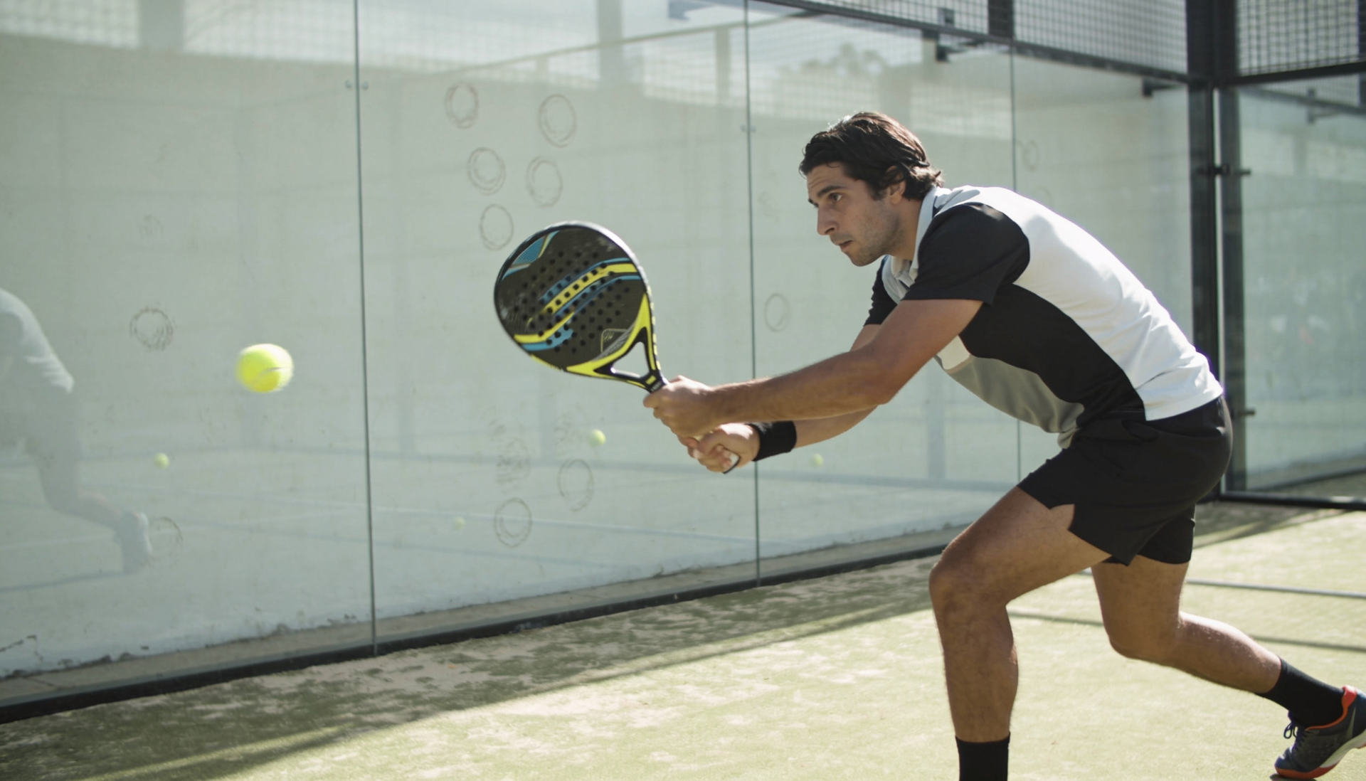 Padel player executing a low backhand volley against the glass on a Dubai padel court